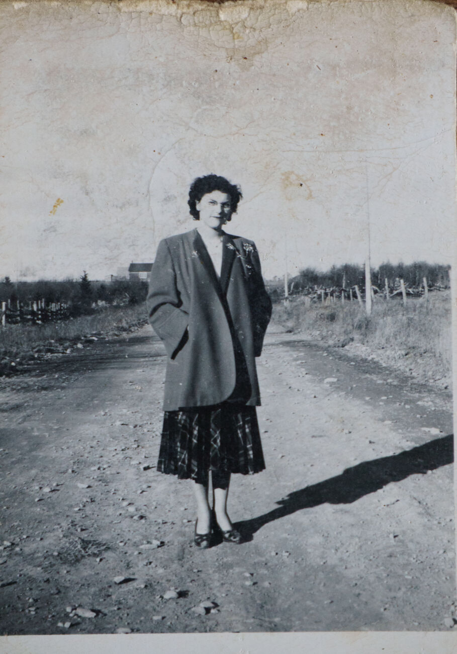 Photo noir et blanc fanée d’une femme marchant sur un chemin de terre, avec rayures et poussière.