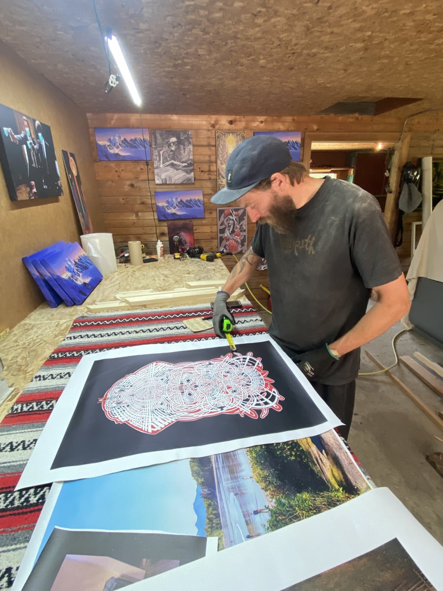 Measuring a fine-art print in the WinPrint shop, finished canvases on the wall behind