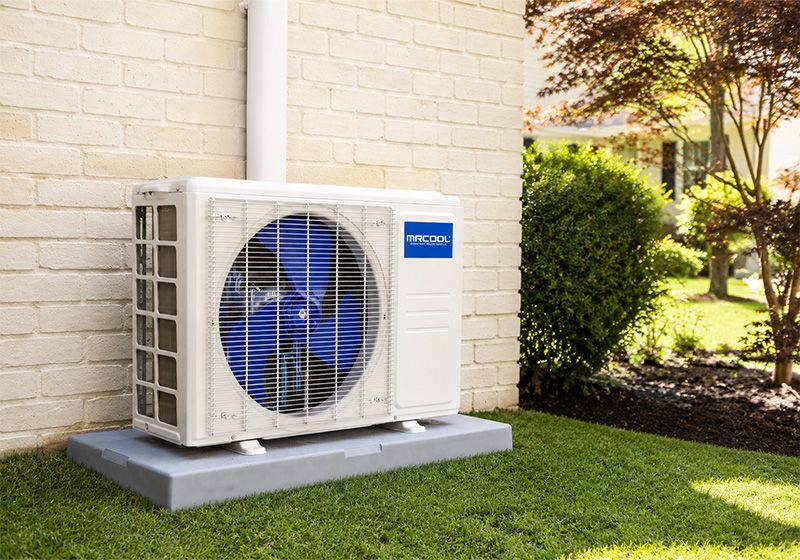 A MRCOOL Condenser on the side of a white brick house