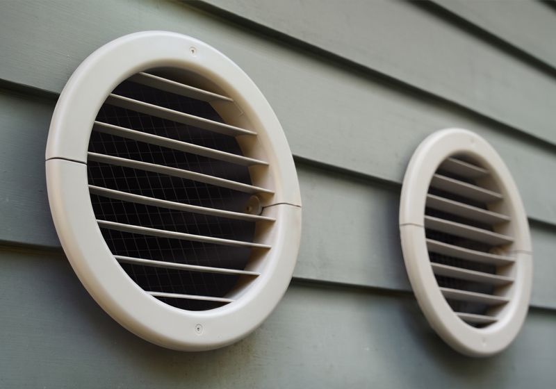 Two white Monoblock MTHP vents on gray home siding.