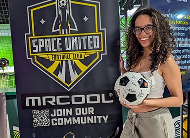 Female youth holding soccer ball next to MRCOOL sponsor of Space United banner