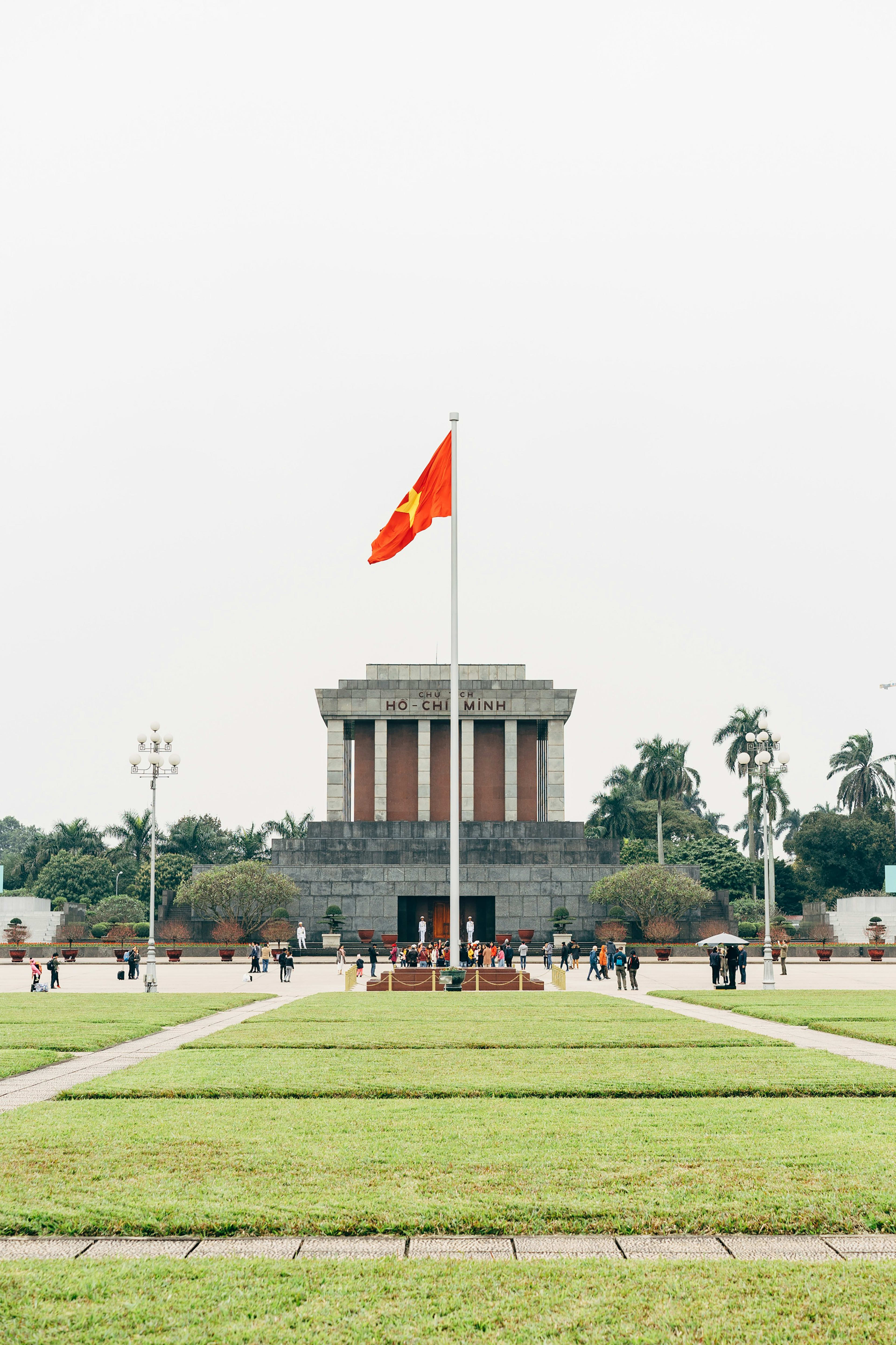 The Hồ Chí Minh Mausoleum seen across the lawns of Ba Đình Square, the Vietnamese flag flying from a tall mast in front of it.