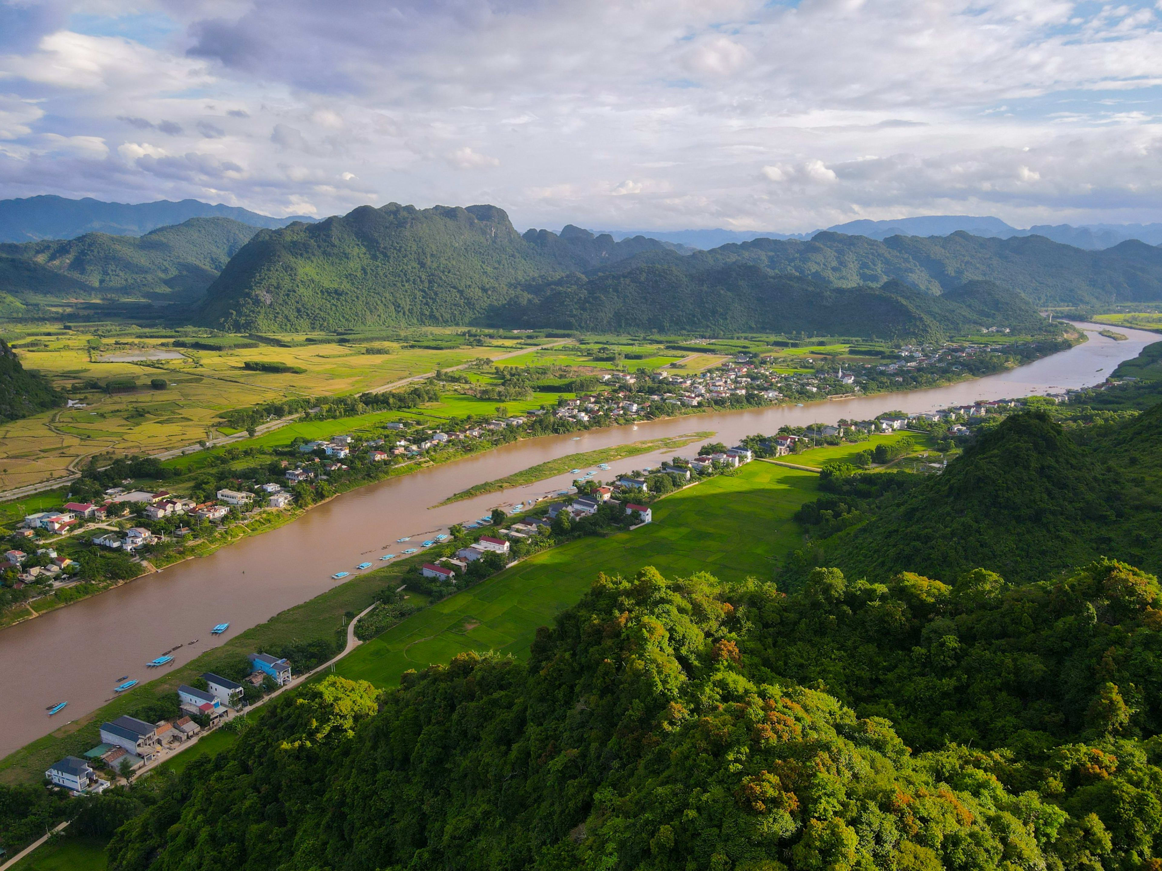 A river curving between karst mountains and paddy fields, villages strung along both banks under towering cloud.
