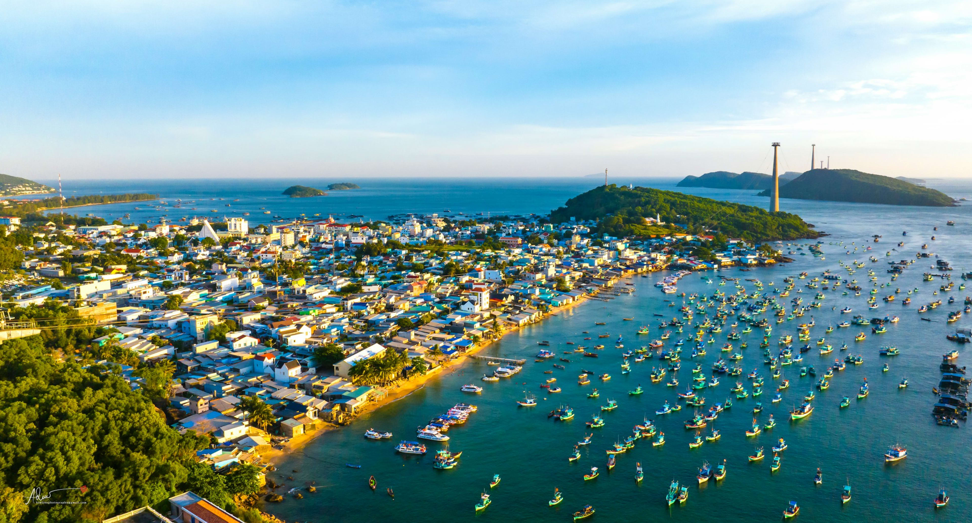 A fishing town from the air with hundreds of blue boats packed into the harbour, a green headland and islands beyond.
