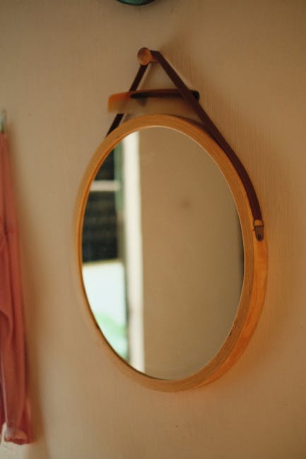 A stylish round wooden mirror mounted on an indoor wall reflecting light.