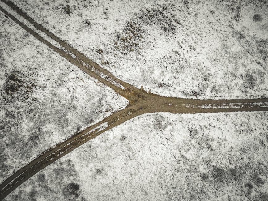 Drone shot of a snowy landscape with a forked dirt road in Bindslev, Denmark.