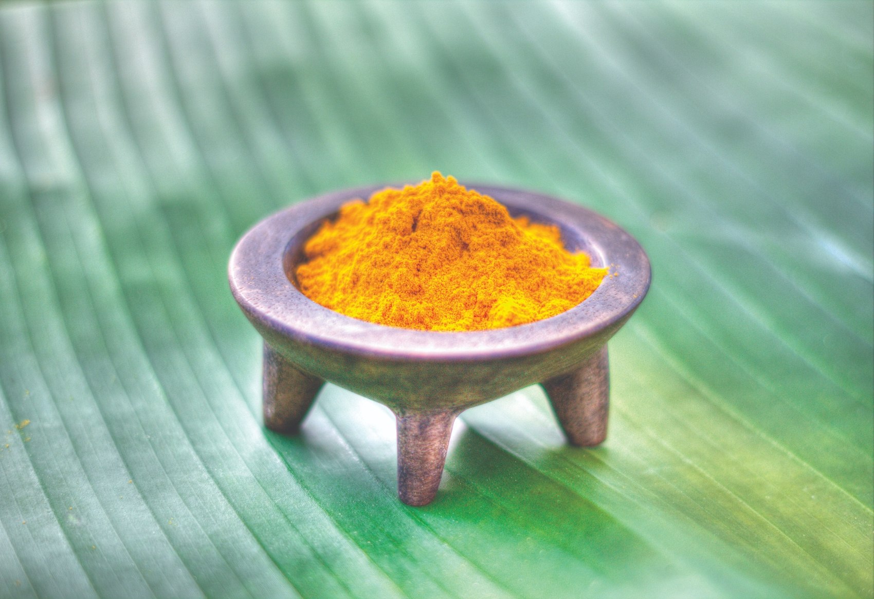 Golden turmeric powder in a small bowl resting on a green leaf.