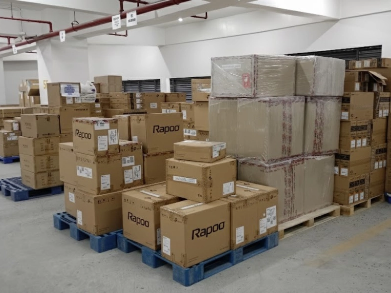Stacks of Rapoo-branded cardboard boxes in a warehouse on blue pallets.