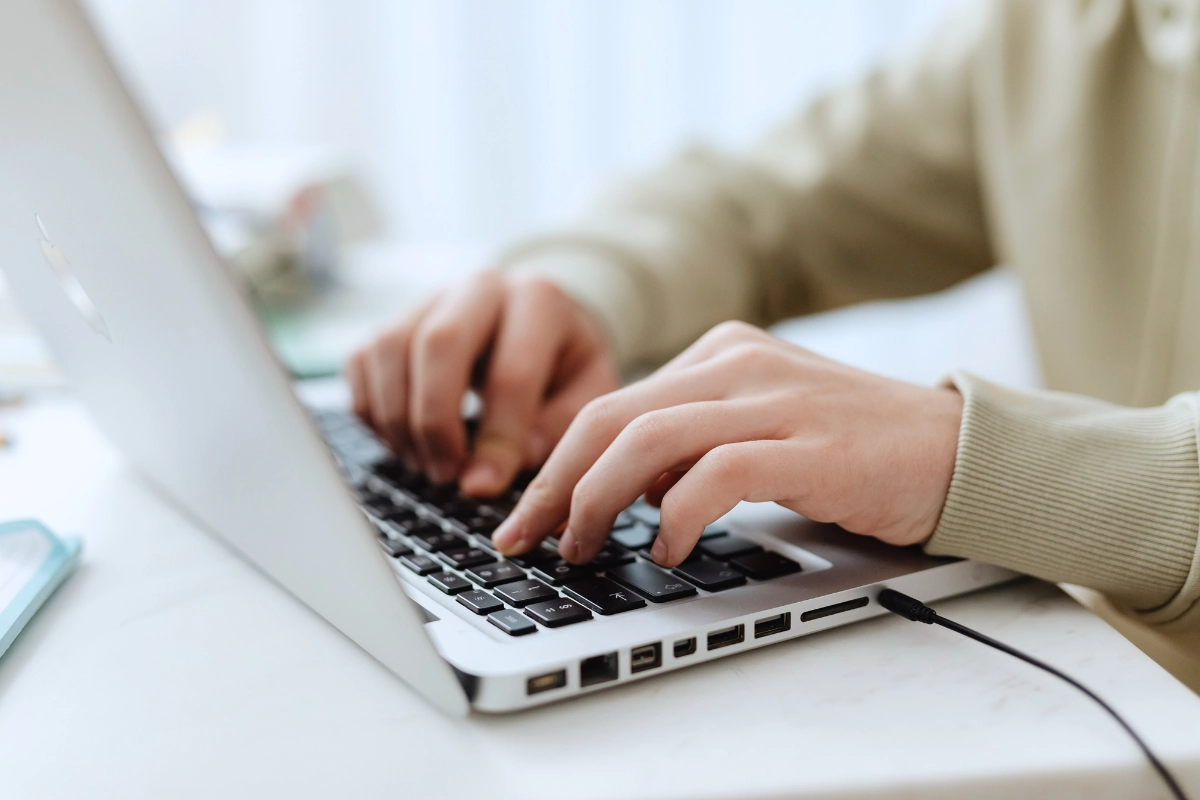 Close-up of a person's hands typing quickly on the black keyboard of a silver laptop, symbolizing work, data entry, or online learning.