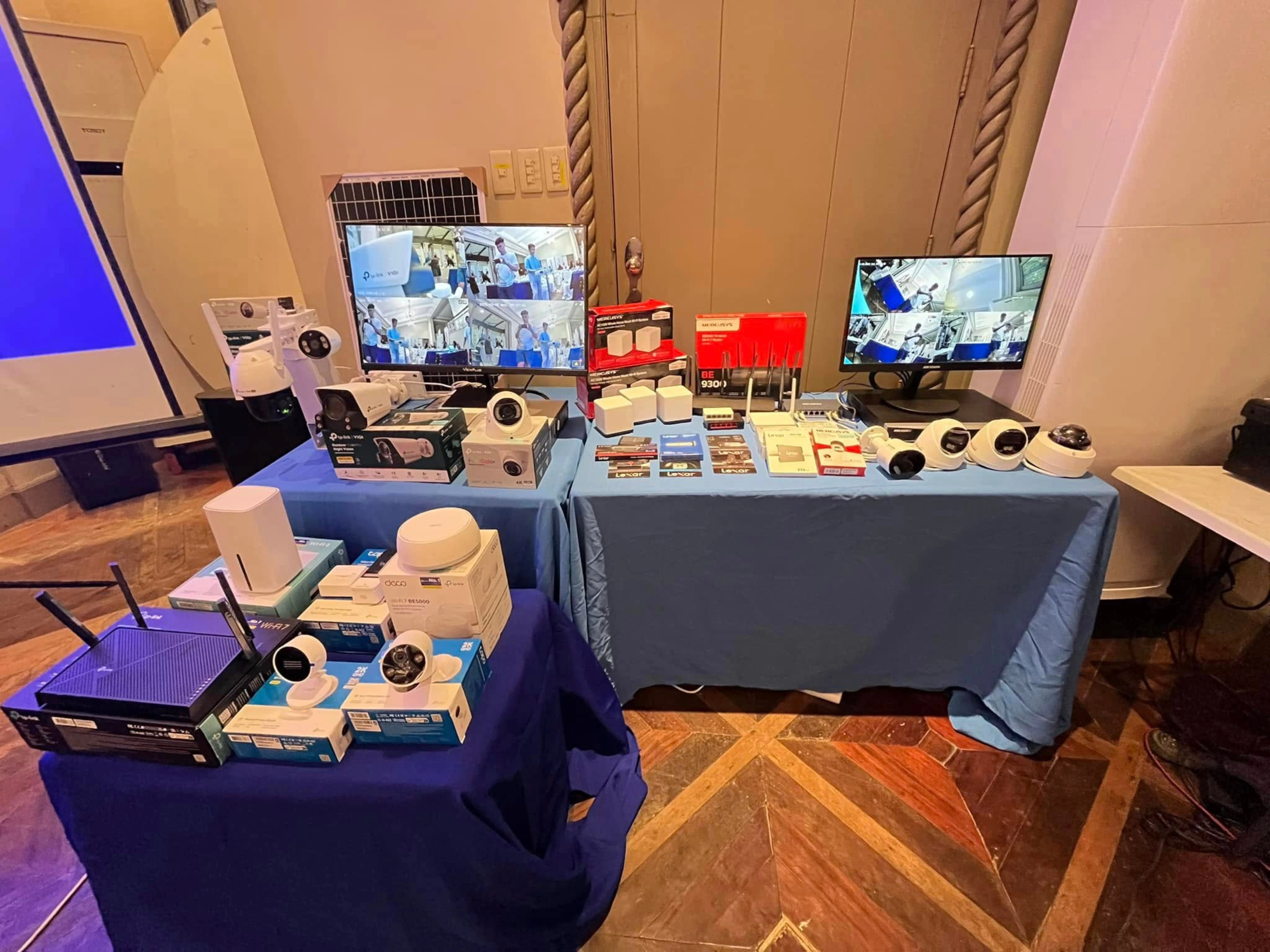 Exhibit table displaying security surveillance cameras, network routers, and monitors for CCTV and smart home solutions.