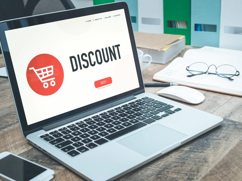 Laptop on a desk displaying a website with the word "DISCOUNT" and a shopping cart icon on the screen.