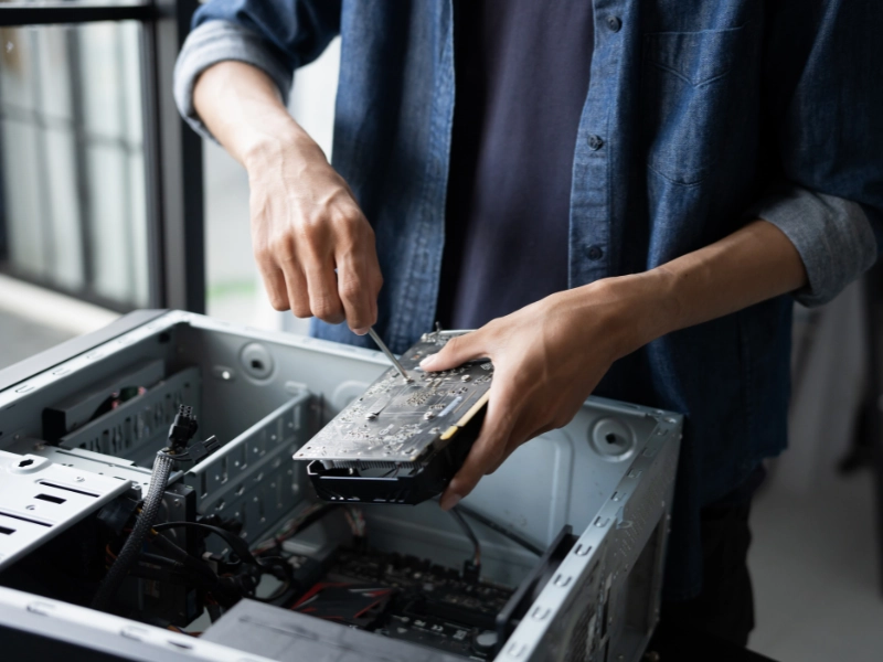A person assembling a desktop PC, using a screwdriver to secure a graphics card inside the computer case.