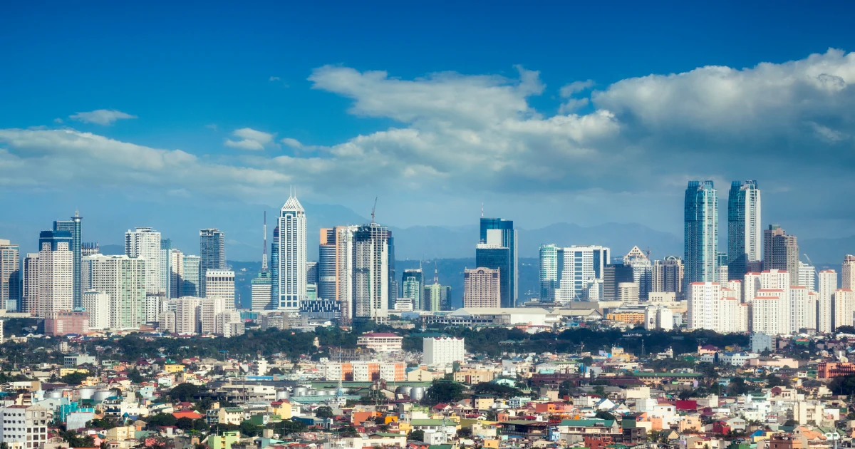 Skyline of a bustling city with modern skyscrapers under a clear blue sky. A mix of colorful low-rise buildings in the foreground, conveying urban vibrancy.