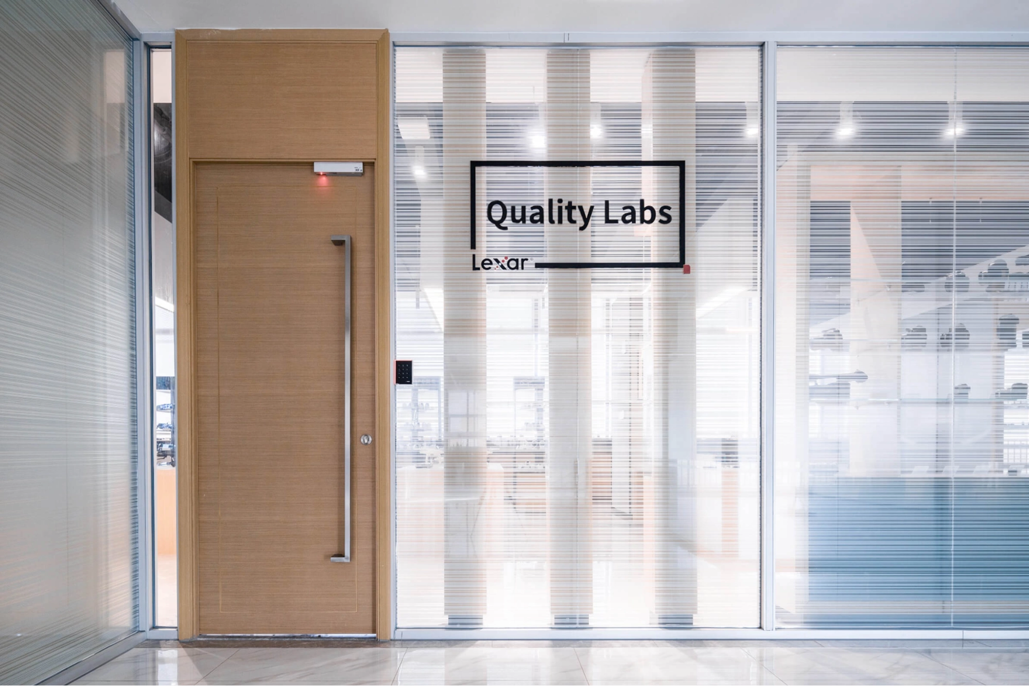Entrance to the Lexar Quality Labs, showing the "Quality Labs" sign on a glass door next to a light wood door.