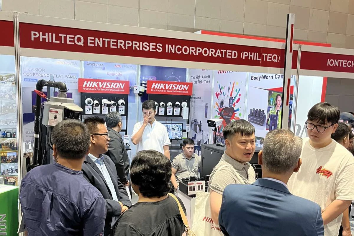 A crowded trade show booth for Philteq Enterprises Incorporated, featuring Hikvision security products. Attendees engage in conversation, creating a lively atmosphere.