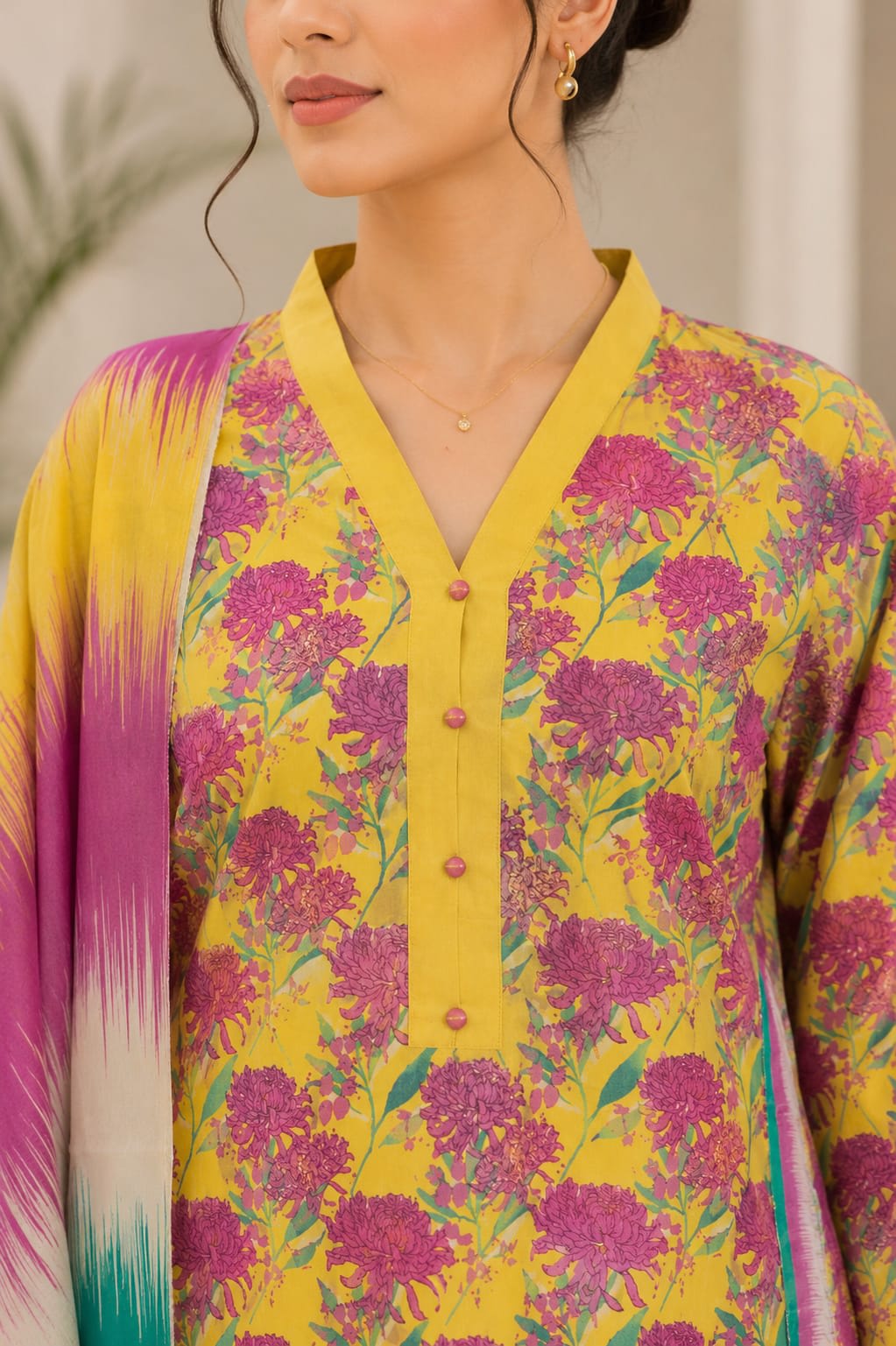 Close-up view of the solid yellow V-neck placket with pink buttons on a yellow dahlia print shirt