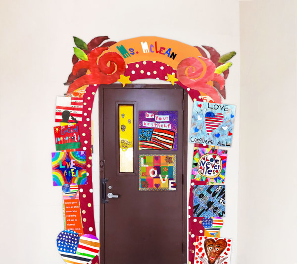 The perimeter of a classroom door is decorated with dozens of square pieces of student artwork. At the top of the archway are multicolored letters that spell the name 'Ms. McClean.'