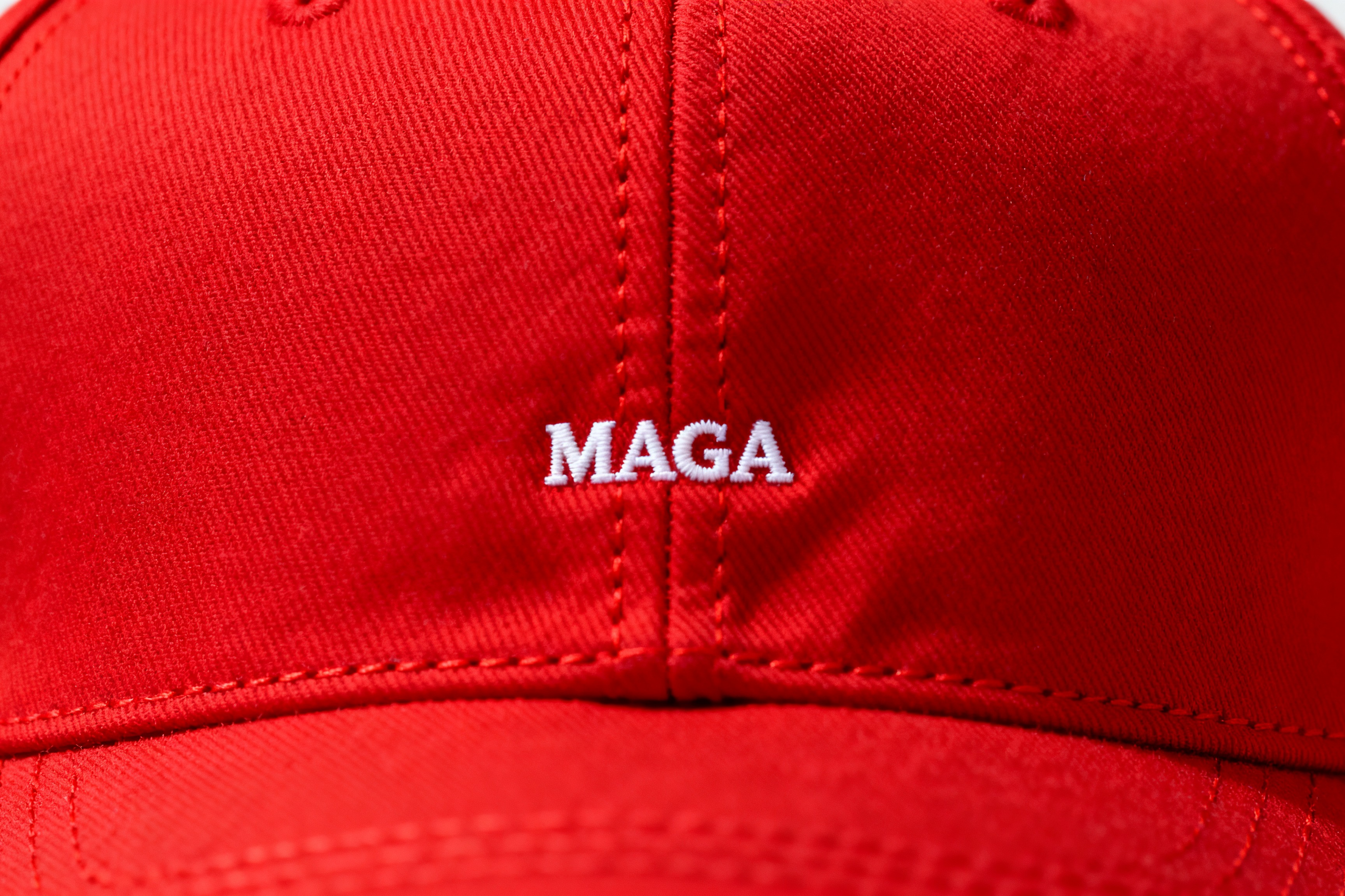 Close-up of a red baseball cap with the word “MAGA” stitched in small white lettering at the centre.