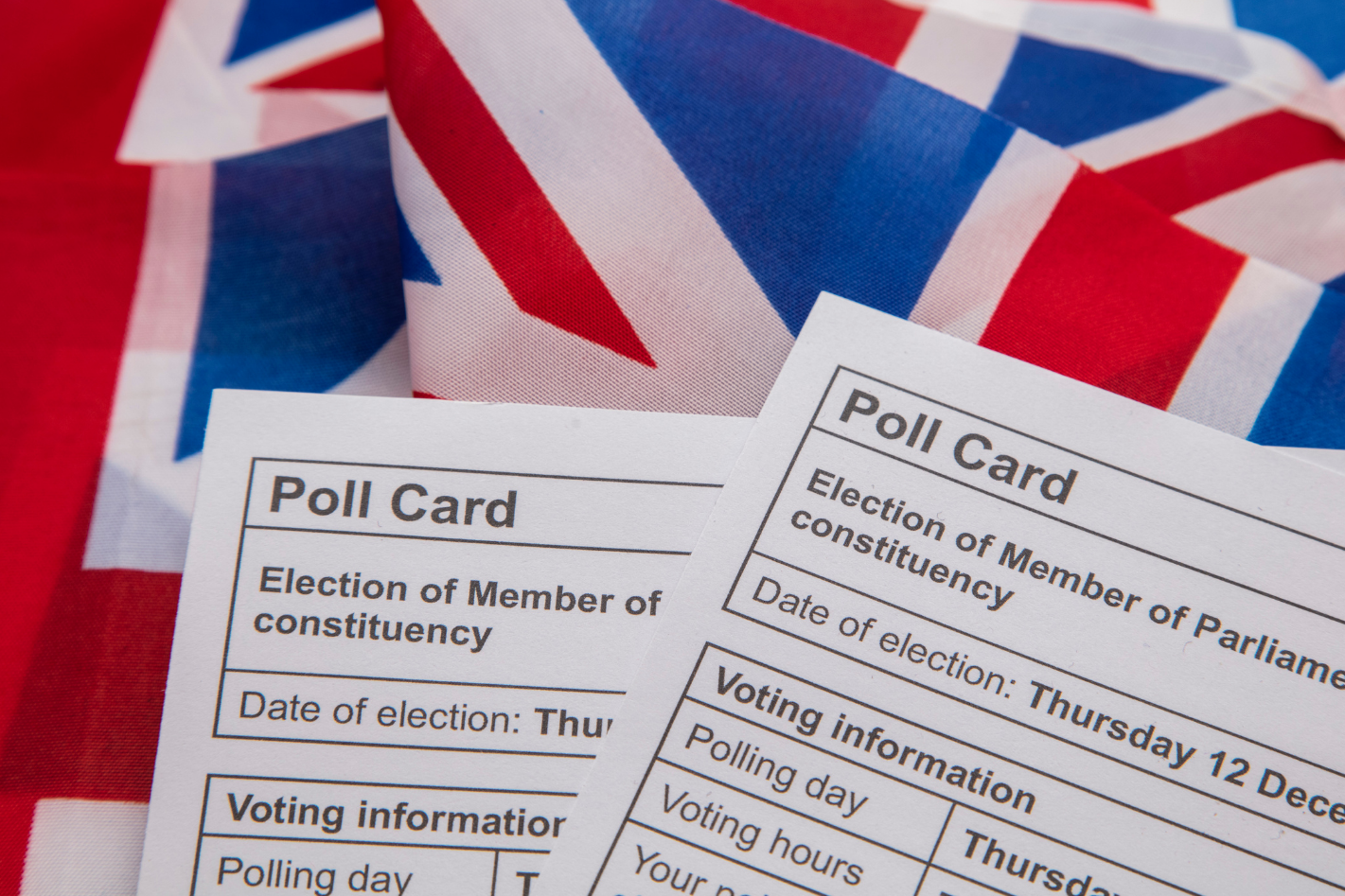 Two UK election poll cards placed on top of a Union Jack flag, representing participation in British parliamentary elections.