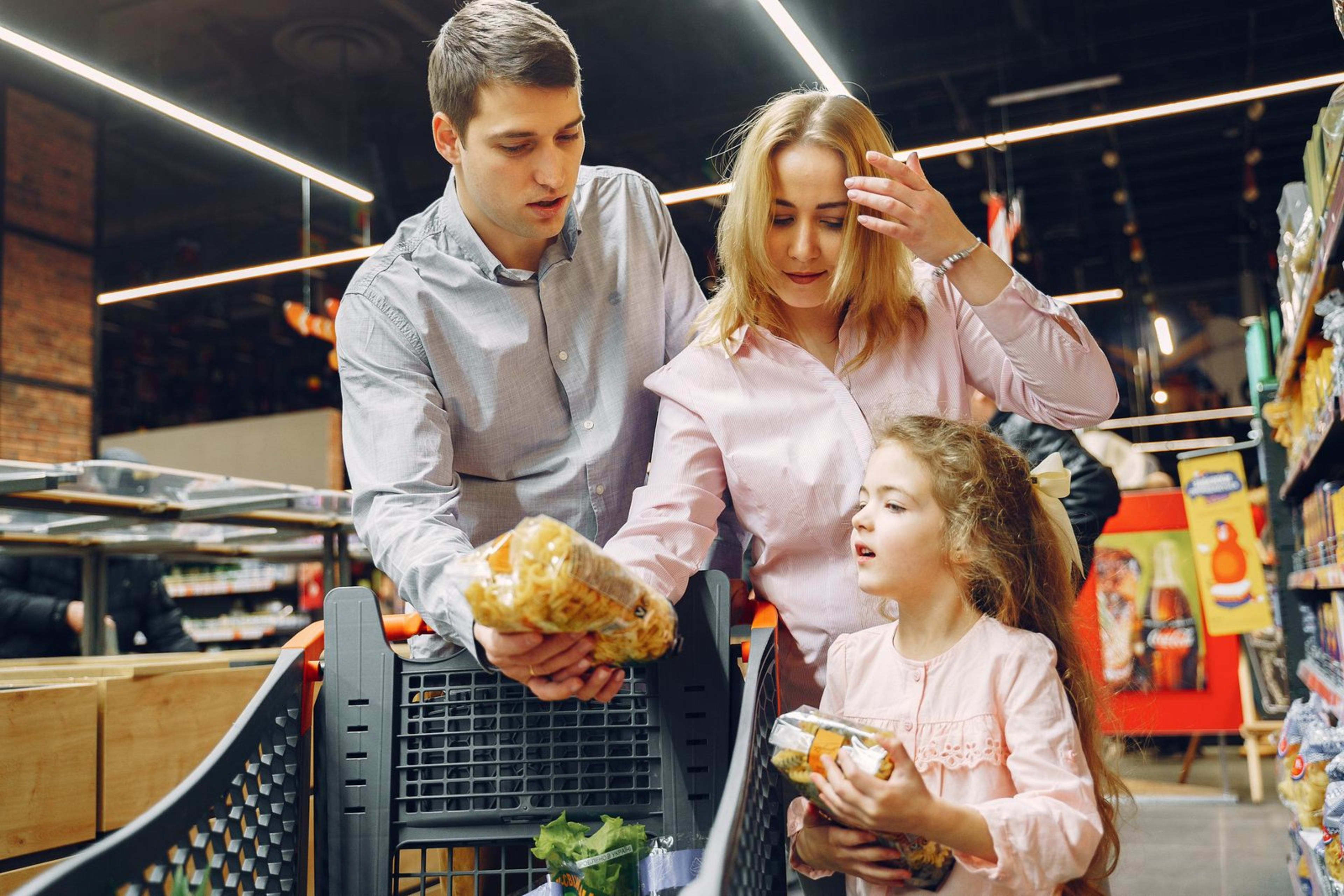 A family shopping for groceries in a supermarket aisle with a cart full of food