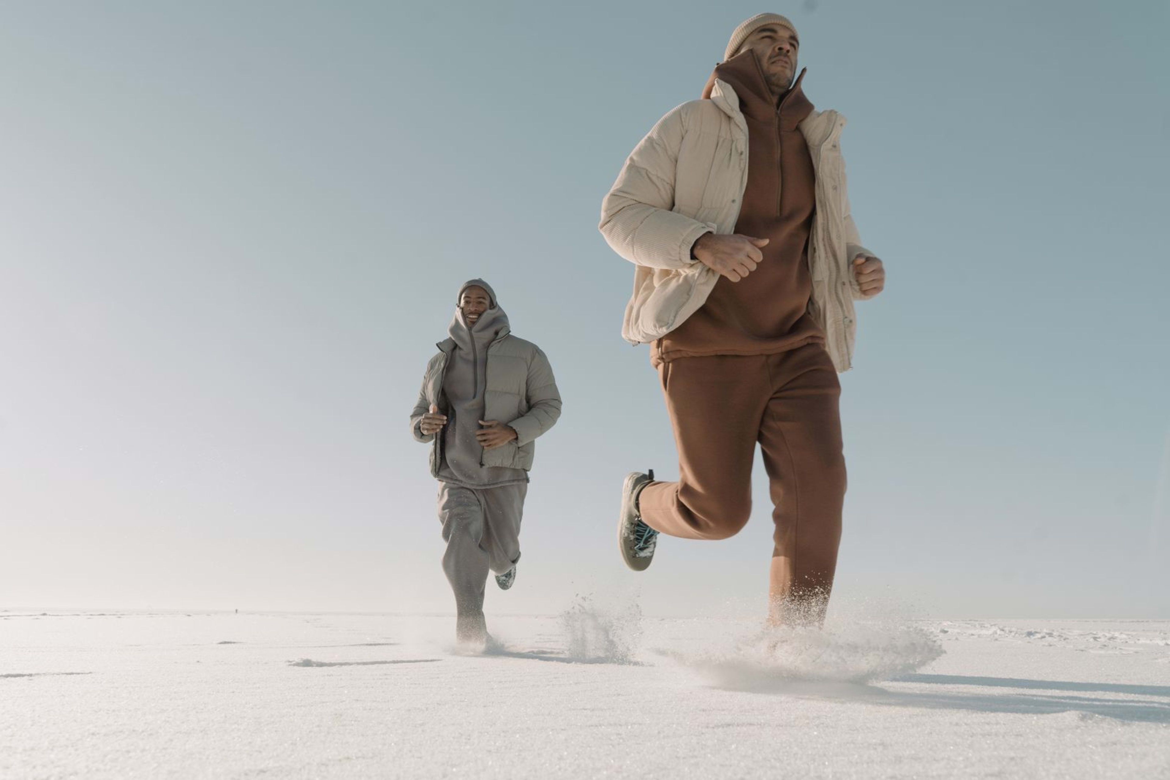 A runner in winter gear jogging on a snow-covered path with visible breath in the cold air