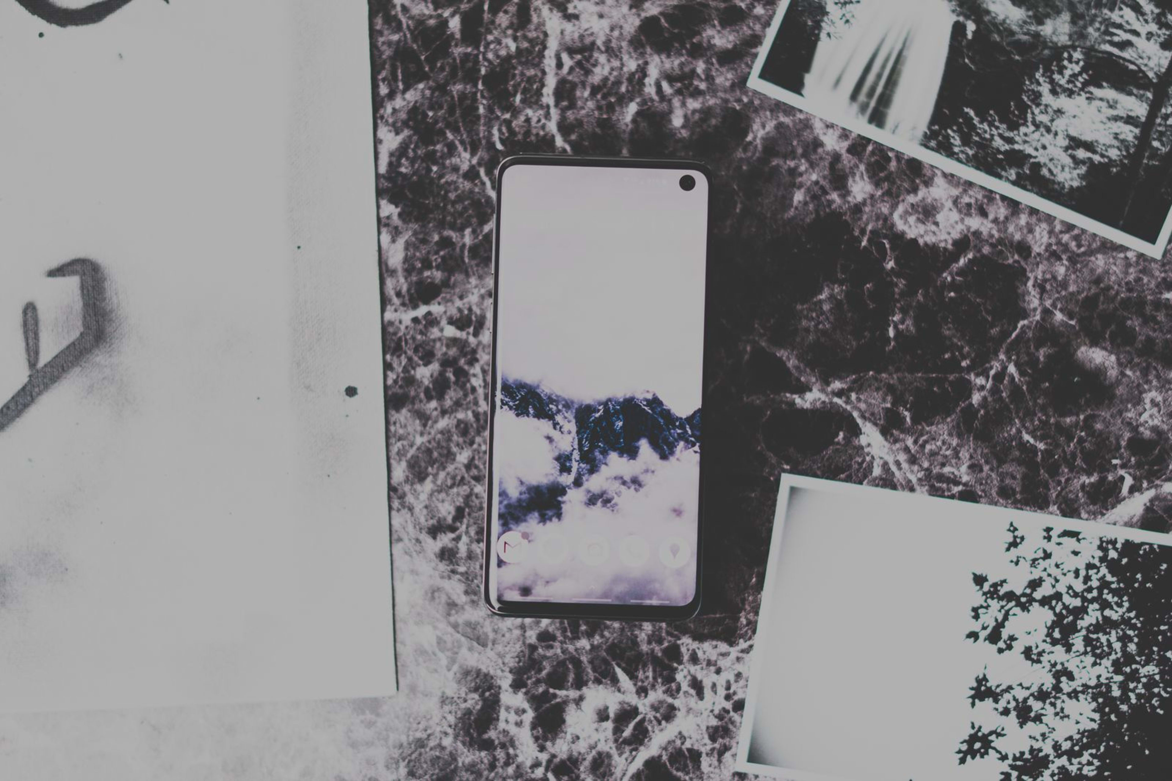 A smartphone lying on a dark marble surface surrounded by black-and-white printed photographs.