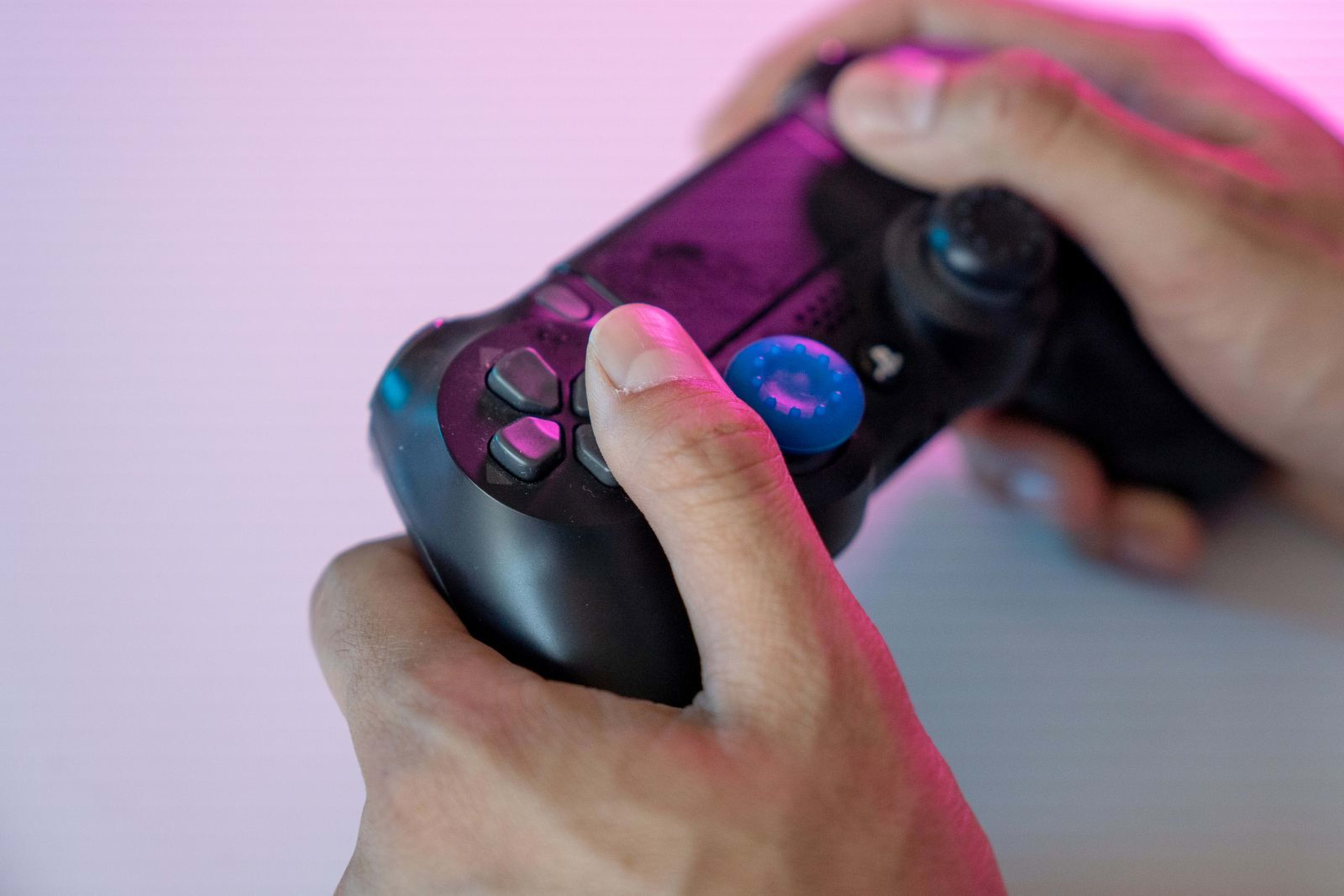 Hands gripping a black gaming controller under pink and purple neon lighting.