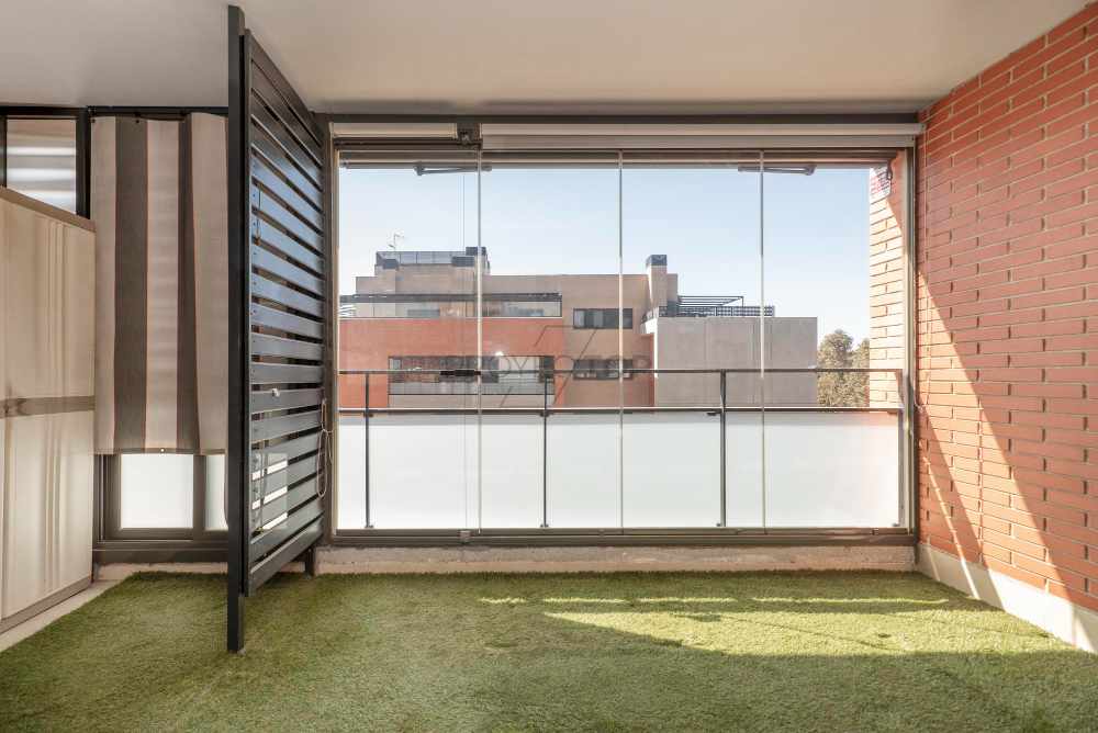 Terraza con paredes de cristal, suelos de césped artificial y barandilla de hierro pintado en una casa residencial urbana