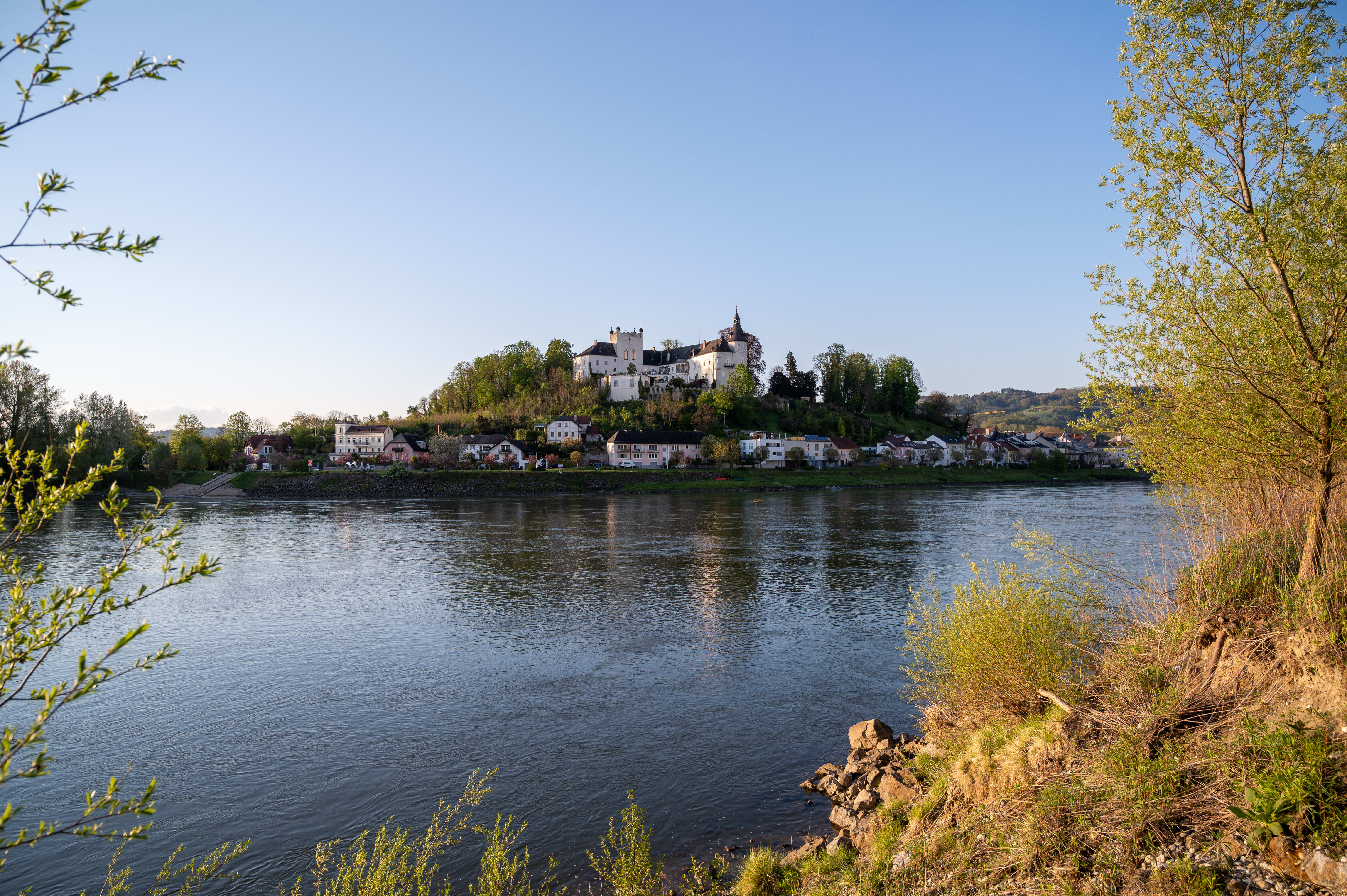 Eine atemberaubende Aussicht auf Ottensheim, die zur goldenen Stunde von Wilhering aus aufgenommen wurde. Die gesamte Stadt erstrahlt in einem herrlichen goldenen Farbton, während die Sonne über den sanften Hügeln untergeht.