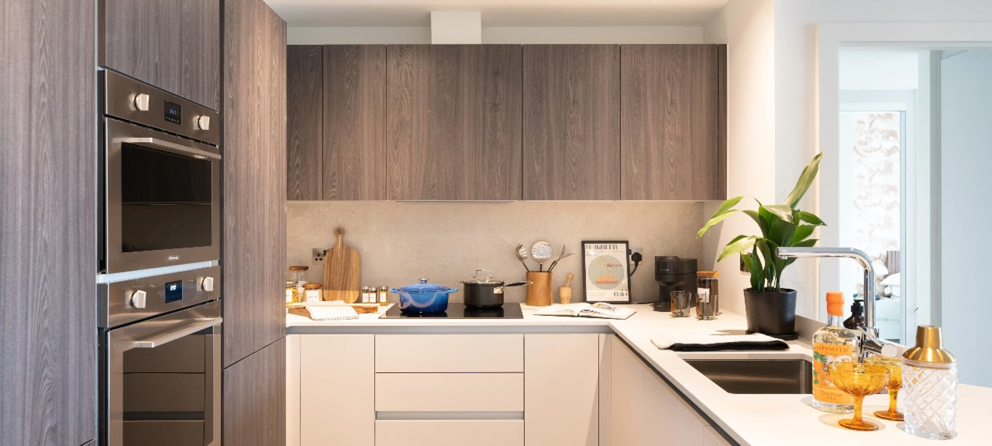 Thumbnail Modern kitchen with wood-paneled cabinets, built-in ovens, and a bright white countertop at Bloom Nine Elms