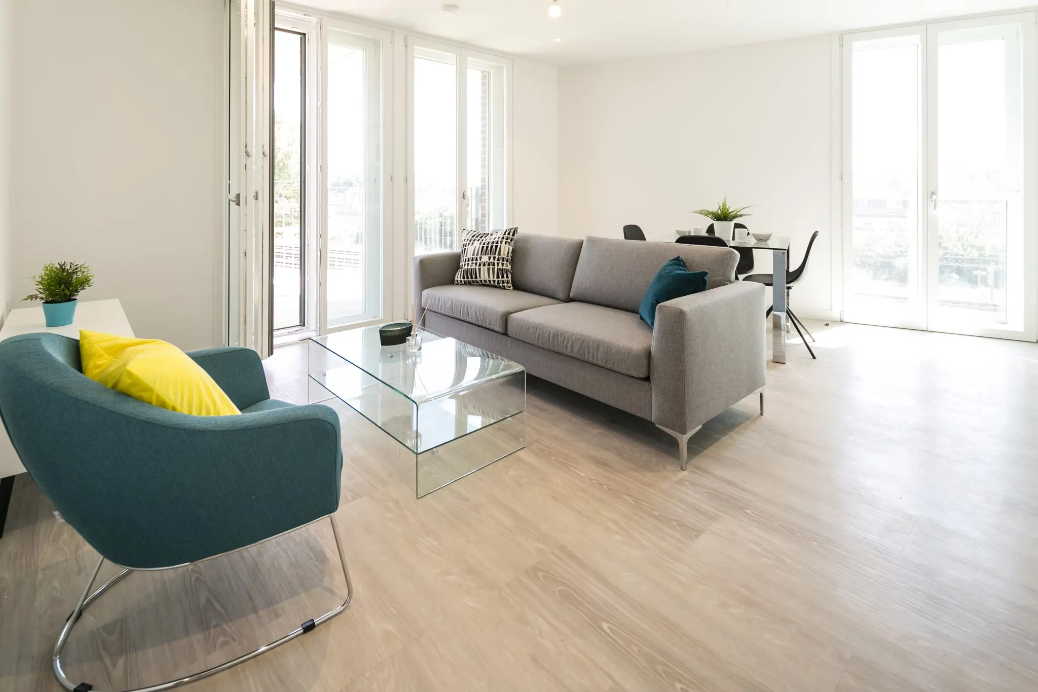 Thumbnail Open-plan living area at Fizzy Hayes with grey sofa, glass coffee table, and teal accent chair near full-height windows