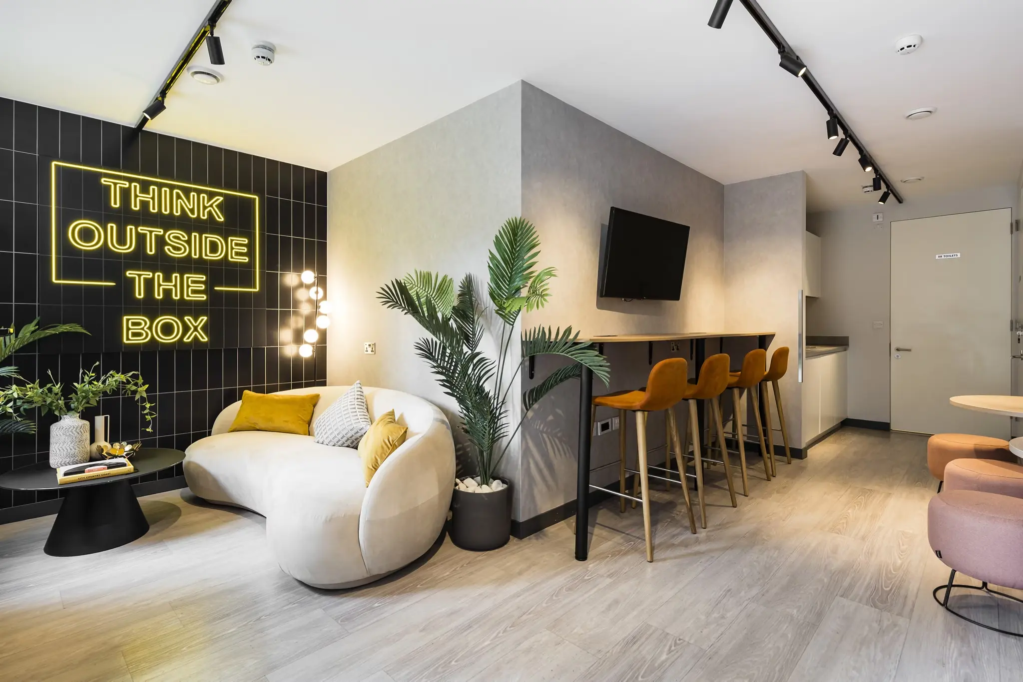 Thumbnail Stylish communal lounge at Fizzy Hayes with curved sofa, neon sign, bar seating, and modern decor