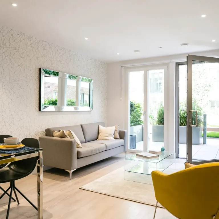 Thumbnail Bright modern living room at Fizzy Hayes with grey sofa, yellow chair, and glass coffee table opening to a garden patio
