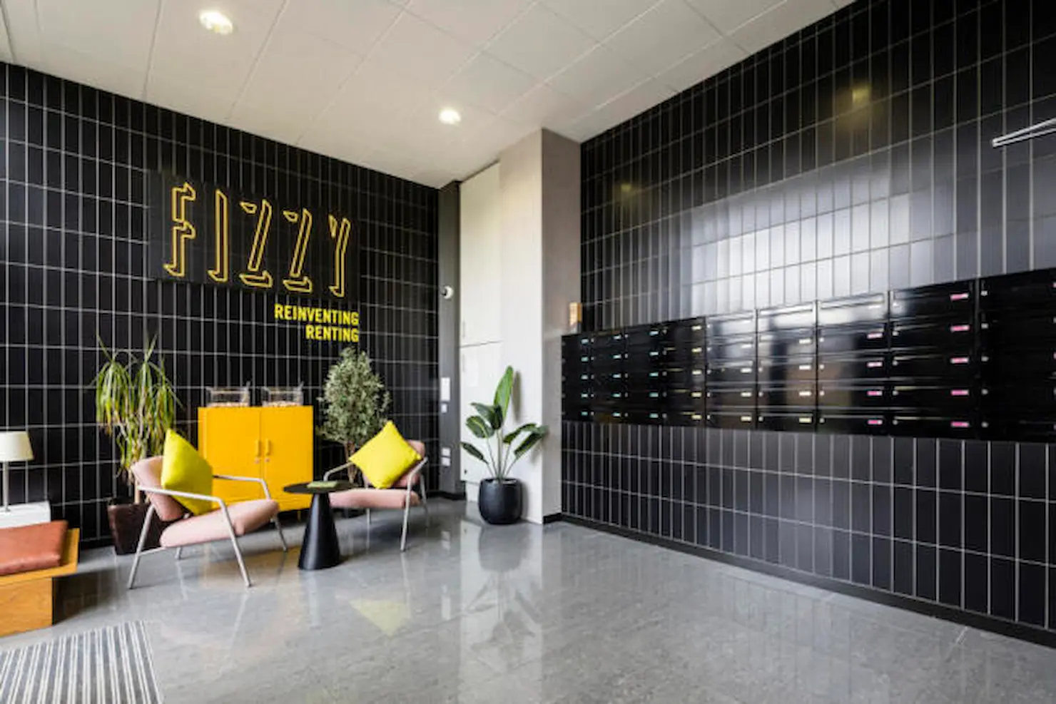 Thumbnail Fizzy Poplar lobby with black tiled walls, mailboxes, yellow cabinet, and modern seating area