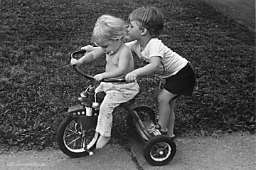 Black and white photograph of two children riding a tricycle