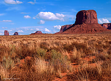 Color landscape photograph of Monument Valley and blue sky with puffy clouds