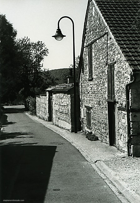 Black and white landscape photograph of street with lamp post and old stone house and geometric shapes