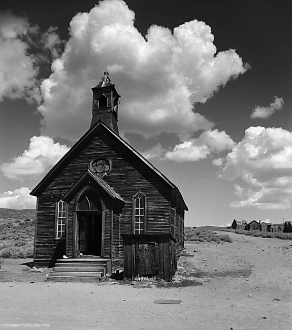 Black and white landscape photograph of old wooden church, and puffy clouded sky