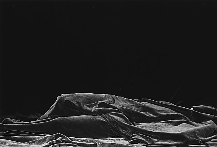 Black and white photograph of a rumpled black blanket with a dark black background