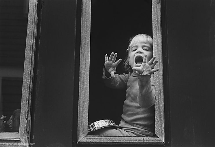 Black and white photograph of a young girl shouting out a window