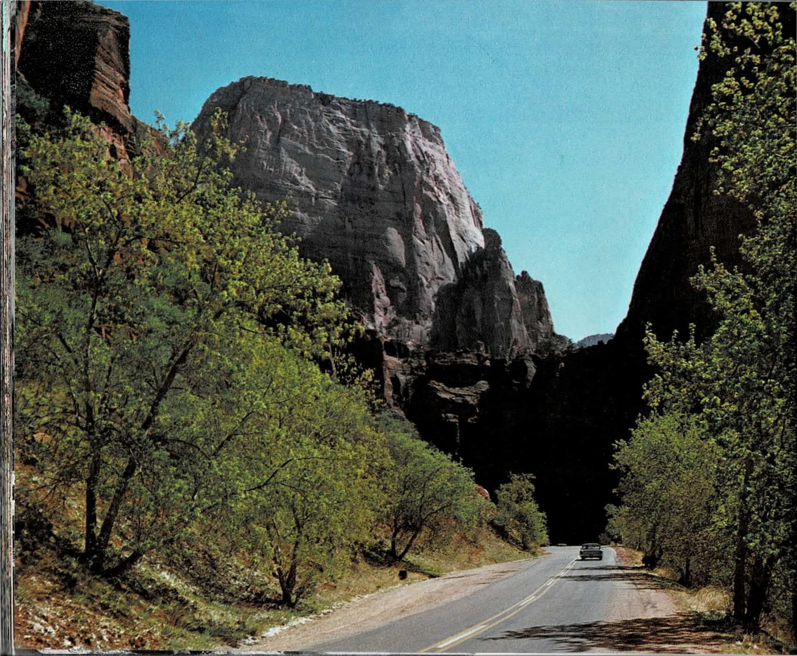Color photograph of a paved two-lane canyon road curving between tall sandstone cliffs and spring-green trees toward a dark tunnel entrance on the left page, facing a black-and-white photograph of a soaring pointed sandstone peak with a natural arch near its base on the right page.