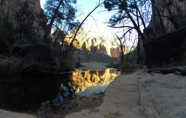 A calm reflective pool below red cliffs near the Emerald Pools trail in Zion