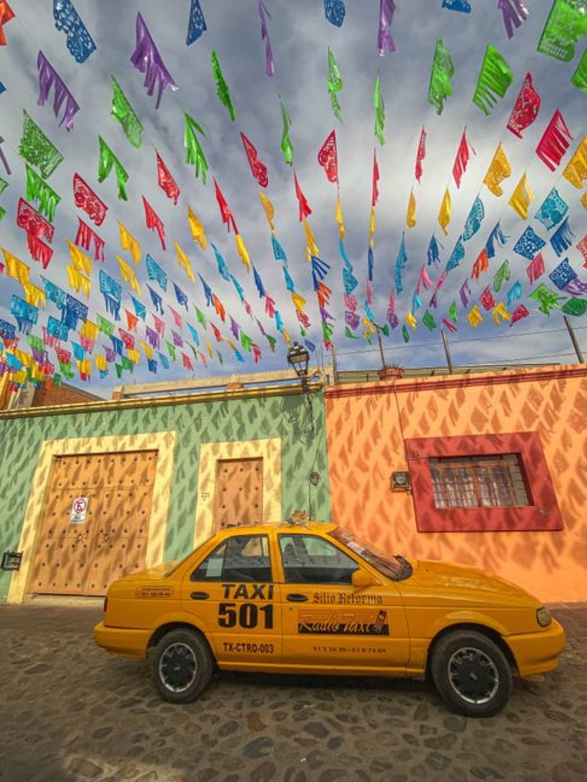 Getting around Puerto Escondido by taxi — colorful Oaxaca street scene with yellow taxi, festive flags and colonial buildings