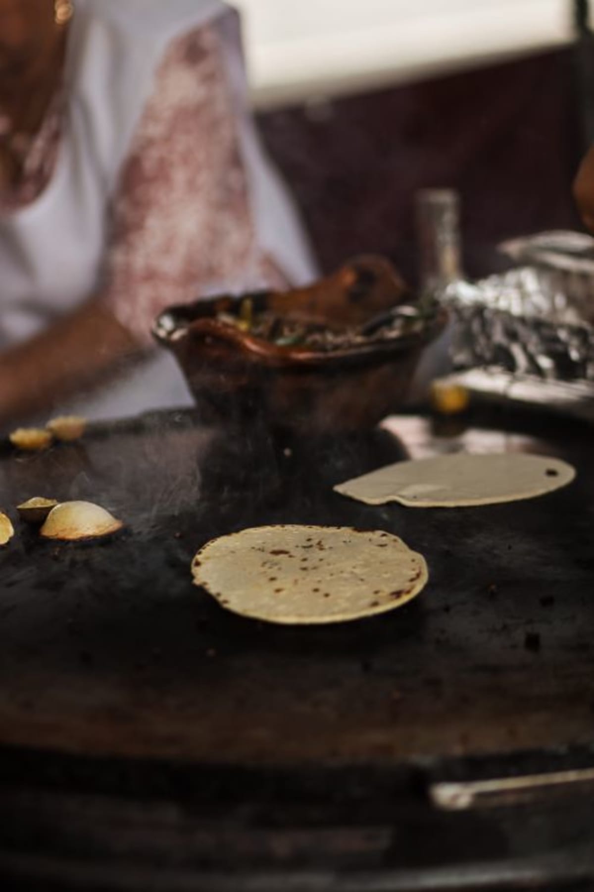Street vendor toasting a large tortilla on a comal for a tlayuda in Oaxaca-style market