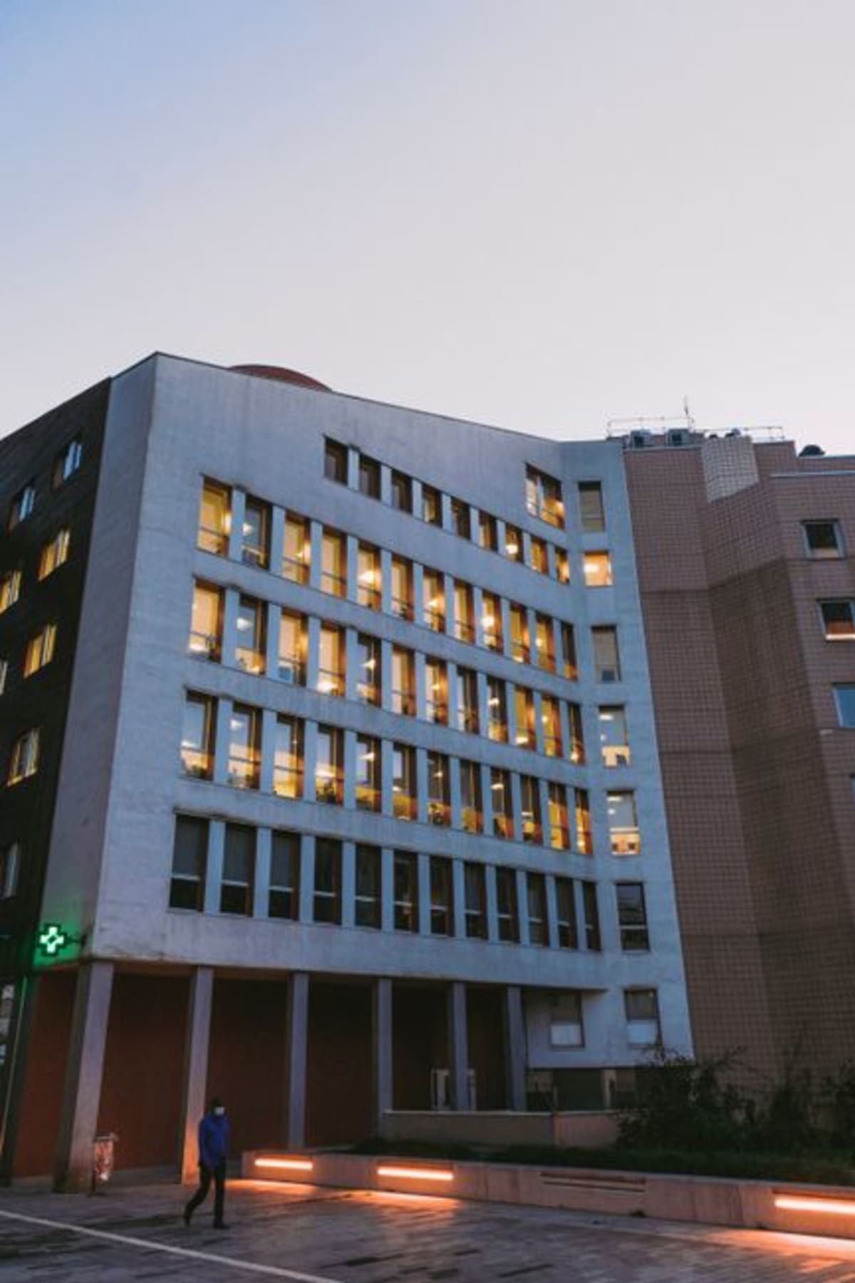 Modern hospital building exterior with illuminated windows at dusk — the Hospital General de Puerto Escondido operates 24 hours for emergencies