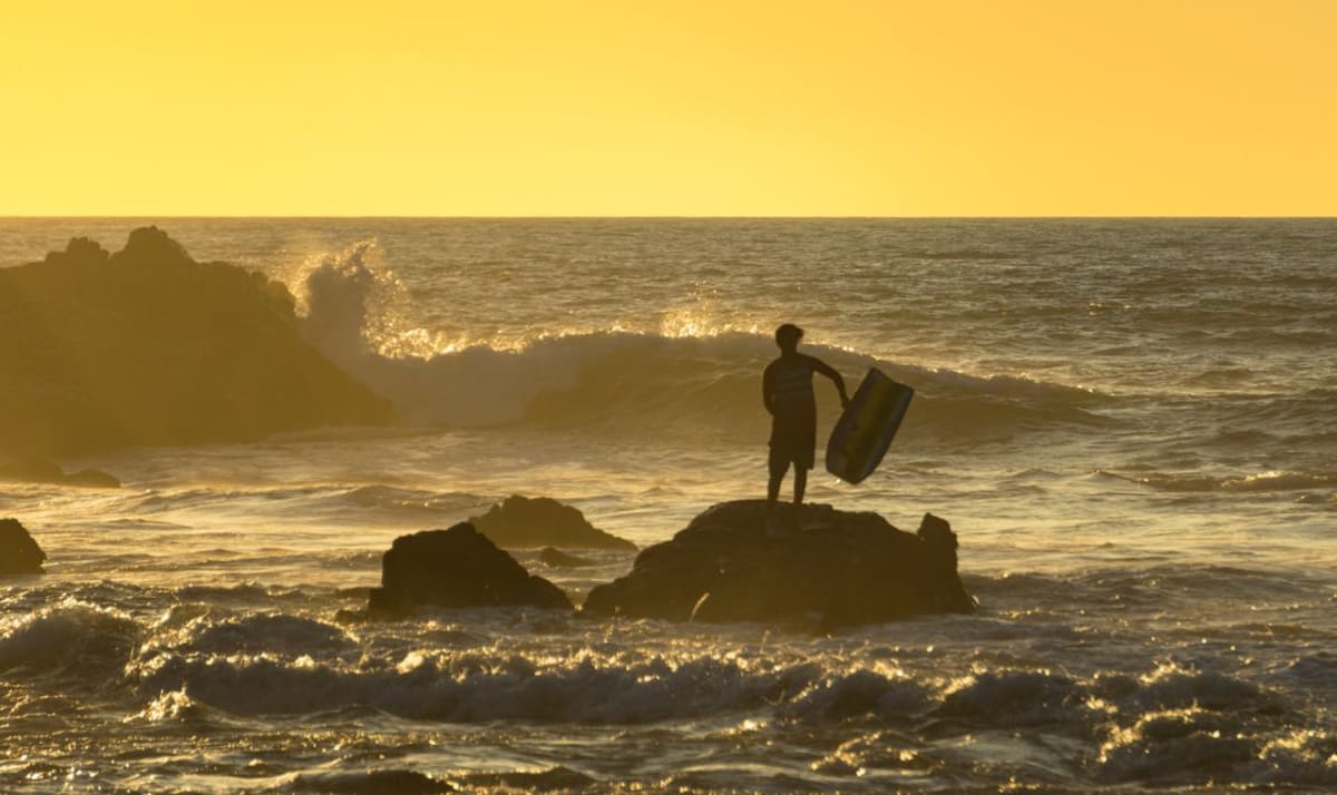 Surfer silhouette at sunset on a rocky beach in Oaxaca, before heading to The Boneyard
