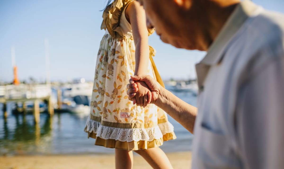 Grandfather holding his granddaughter's hand on a walk by the sea during a family trip