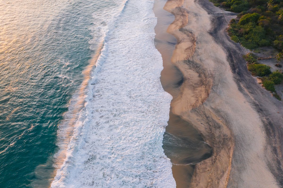Vista aérea de las olas del Pacífico rompiendo sobre una playa oaxaqueña salvaje