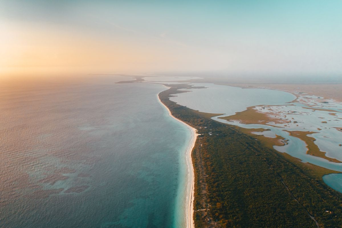 Vista aérea de una playa durante el atardecer con cielo dorado y océano tranquilo en México
