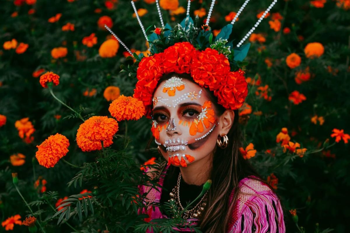 Frau mit traditioneller schwarz-weißer Día de Muertos Gesichtsbemalung umgeben von leuchtend orangen Cempasúchil-Ringelblumen
